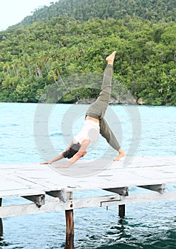 Girl exercising yoga pose three-legged downward dog on jetty by sea