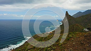 Girl explores mountains overlooking the blue endless ocean in cloudy day. Green sea coastline. Rock of the Souls in