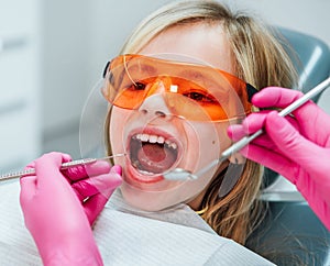 girl in eyeglasses sitting in stomatology chair while female dentist\'s palms in pink gloves with excavator and