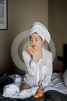 Girl with eyes closed and with towel on head and fruit in hend in the morning sitting on bed.