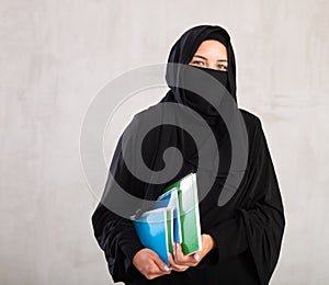 girl with face covered with burka holds lot of thick notebooks. foreign