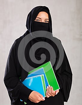 girl with face covered with burka holds lot of thick notebooks. foreign