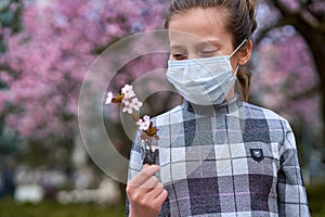 Girl with a face mask is in the city outdoor, blooming trees, spring season, flowering time - concept of allergies and health