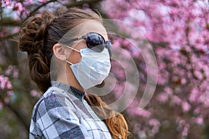 Girl with a face mask is in the city outdoor, blooming trees, spring season, flowering time - concept of allergies and health