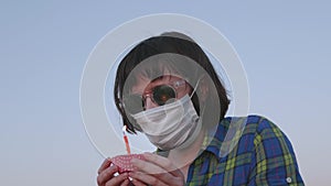 Girl in face mask tries to put out candle on cupcake against blue sky.