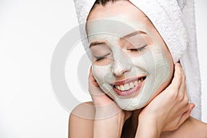 Girl with facial nourishing mask and towel on head touching face with closed eyes isolated on white