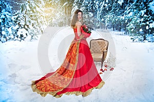 A girl in a fairy-tale image of a queen poses in a snow-covered winter forest.