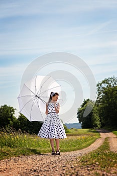 Girl in the Fashion of the fifties und sixties posed with a sunshade in the nature