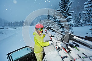 Girl fastening skis on car roof in the evening