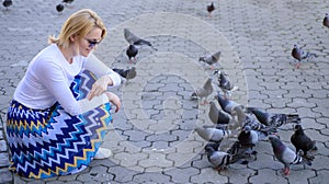Girl feeding dove birds. Group doves on city square waiting treats. Share generosity. Girl blonde woman relaxing city
