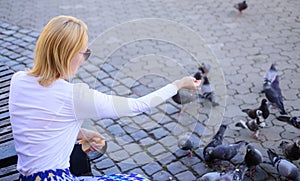 Girl feeding dove birds urban background. Girl blonde woman relaxing city square and feeding pigeons. Woman tourist or