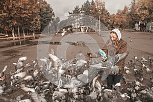 Girl feeding pigeons in the town square .