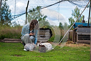 girl feeding rabbits with grain from a plastic cup on farm