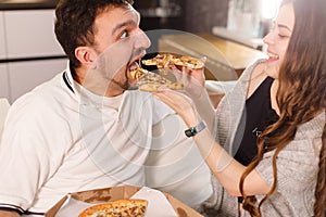 Girl feeds her husband with two slices of pizza. Exaggerate and wondering. Much credit on yourself and capabilities