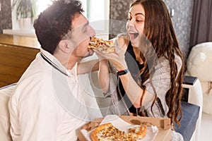 Girl feeds her husband with two slices of pizza. Exaggerate and wondering. Much credit on yourself and capabilities