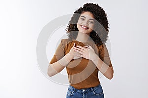 Girl feel grateful thanks bottom heart. Attractive cheerful curly-haired modern young woman hold hands chest thankful