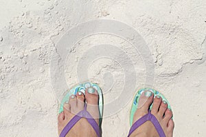 Girl feet in blue slippers on sand beach texture. Tropical seashore. Seaside banner template with text place.