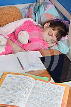 Girl fell asleep in a hug with a teddy bear doing lessons at home