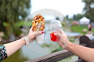 The girl and fella during the walk holds in hands a paper cup with a Belgian waffle and fresh drink on a background of green park photo