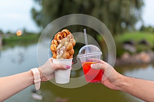The girl and fella during the walk holds in hands a paper cup with a Belgian waffle and fresh drink on a background of green park photo