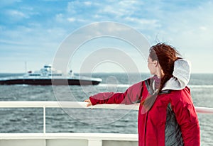 The girl on the ferryboat looks towards the sea, where the liner floats