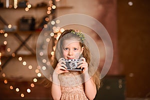 girl in a festive dress with flowing hair holds a vintage camera in her hands, New Year& x27;s garland lamps give yellow bokeh