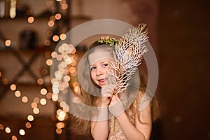 girl in festive dress with flowing hair peeks out from behind golden decorative twig, New Year& x27;s garland lamps give yellow