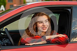 A girl with fiery red hair wears a red shirt and gazes thoughtfully through the car window