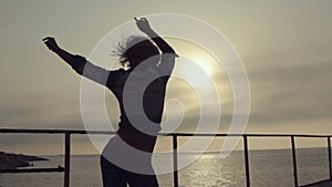 Girl with a figure and short hair incendiary dancing on the pier near the sea at sunset