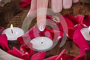 Girl finger with french nails polish style touch candle in bowl with water and red rose petals