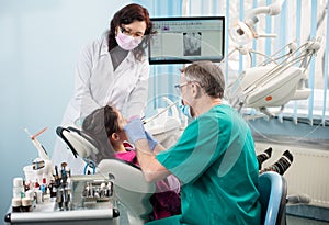 Girl with on the first dental visit. Senior pediatric dentist with nurse treating patient teeth at the dental office