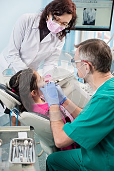 Girl with on the first dental visit. Senior pediatric dentist with nurse treating patient teeth at the dental office