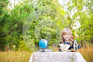 The girl is a first grader sitting at a table and holding an open book in her hands. A schoolgirl in a blue suit and curly hair