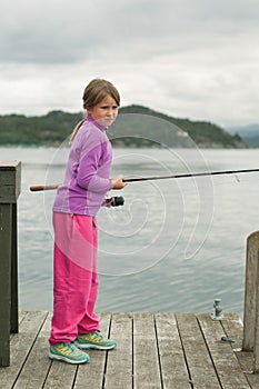 A girl with a fishing rod standing on the wooden deck near water