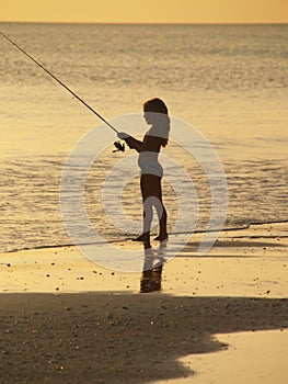 Girl fishing on sunset beach