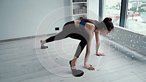 Girl fitness trainer stretching their legs on gym floor using gliding disk