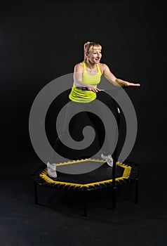 Girl on a fitness trampoline on a black background in a yellow t-shirt yellow fit jump, equipment health vitality, club