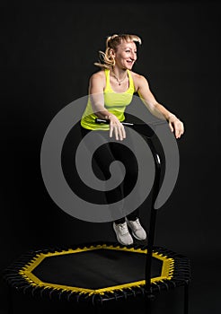 Girl on a fitness trampoline on a black background in a yellow t-shirt trampoline energy jump, active activity female