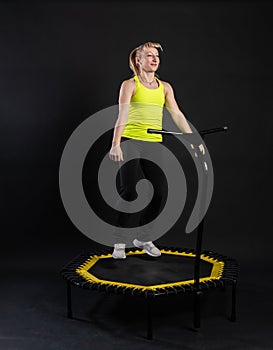 Girl on a fitness trampoline on a black background in a yellow t-shirt trampoline fit sport, activity training girl