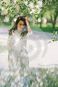 Girl fixes her hair under blooming apple tree