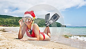 A girl with flippers in an underwater mask and a santa hat lies on the seashore. New Year holidays.
