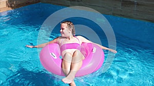 Girl floating on pink inflatable ring in swimming pool. Traveling and vacation concept