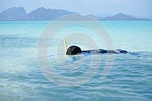 A girl is floating on the surface of the sea and sees the reef and fish under the water by snorkel mask