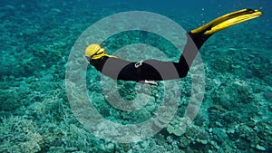 Girl floating under water. Elegant woman in black wetsuit and yellow fins diving into depths. Flexible scuba diver