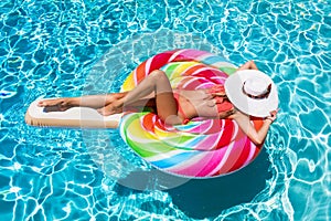 Girl floats on a lollipop shaped float over blue swimming pool water