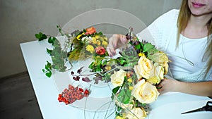 Girl florist picks up flowers for bride`s bouquet and creates floral work sitting at table in office.n