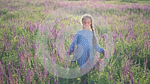 Girl in flower field. Child touches blue flowers with his hand. Girl in blue dress. Child hand touches flowers. Happy