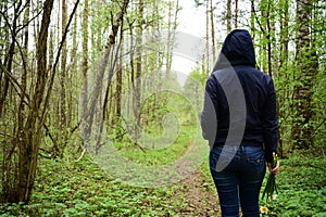 Girl with flowers on a path in the forest. The grass is green near tall slender trees. Young trees stately row. In the middle