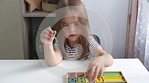 A girl with flowing hair sits at a white table and learns numbers with the help of a board game. Preschool education at