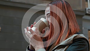 Girl with foxy hair drinking tea in paper cup on the street